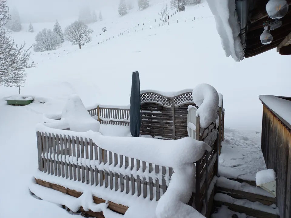 Verschneite Terrasse mit Zaun, Sichtschutz und zugeklapptem Sonnenschirm