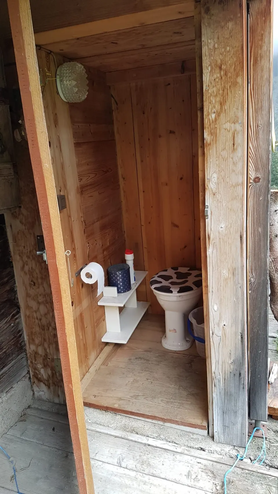 Aussen-WC mit Keramikschüssel, Deckel mit Kuhmuster und Regal mit WC-Papier