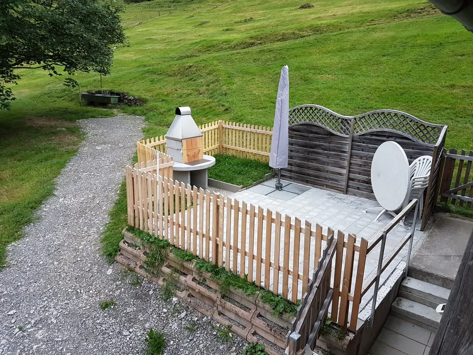 Gepflasterte Terrasse mit Sonnenschirm, Tisch, Stuhl, Sichtschutz und Gartencheminée