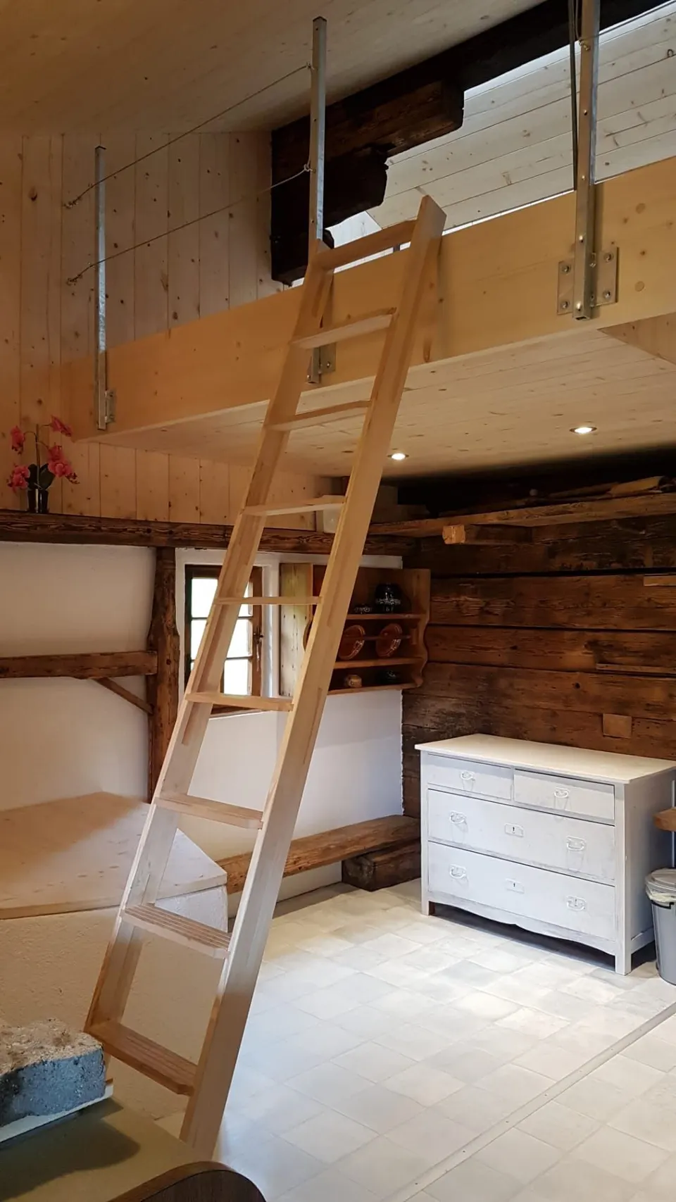 Eingangsraum mit Holzleiter zur Schlafgalerie, weisser Kommode und Plattenboden