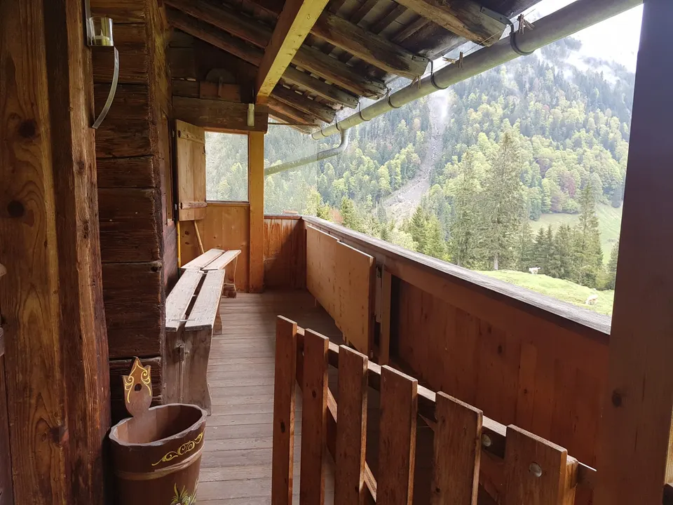 Gedeckte Holzlaube mit Sitzbank, Blick auf einen bewaldeten Hang